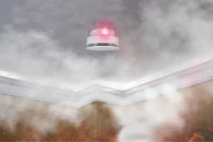 Smoke detector with red light strobing in a smoke-filled room.